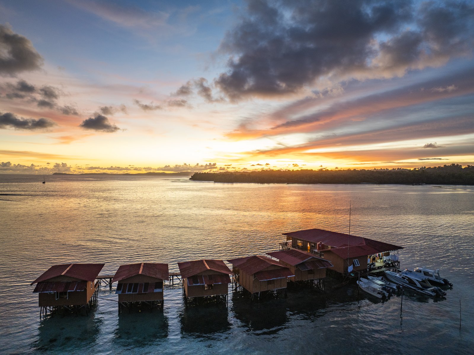 The overwater villas, boats and forested coastline seen from a drone at sunset